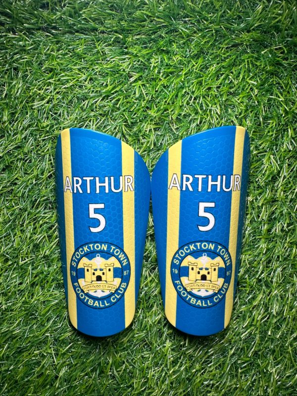 Standard personalised shin pads yellow and blue backdrop with grassroots logo.