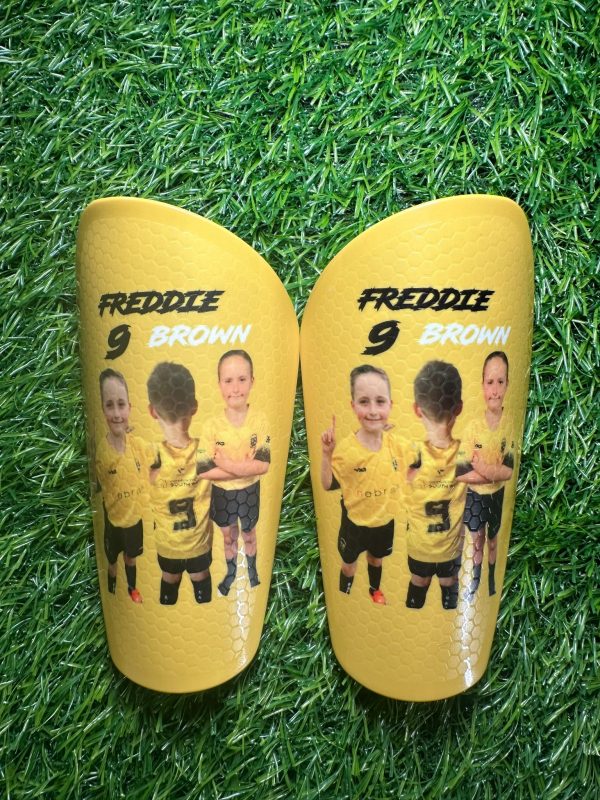 Standard personalised shin pads. Yellow backdrop with players and white and black text.