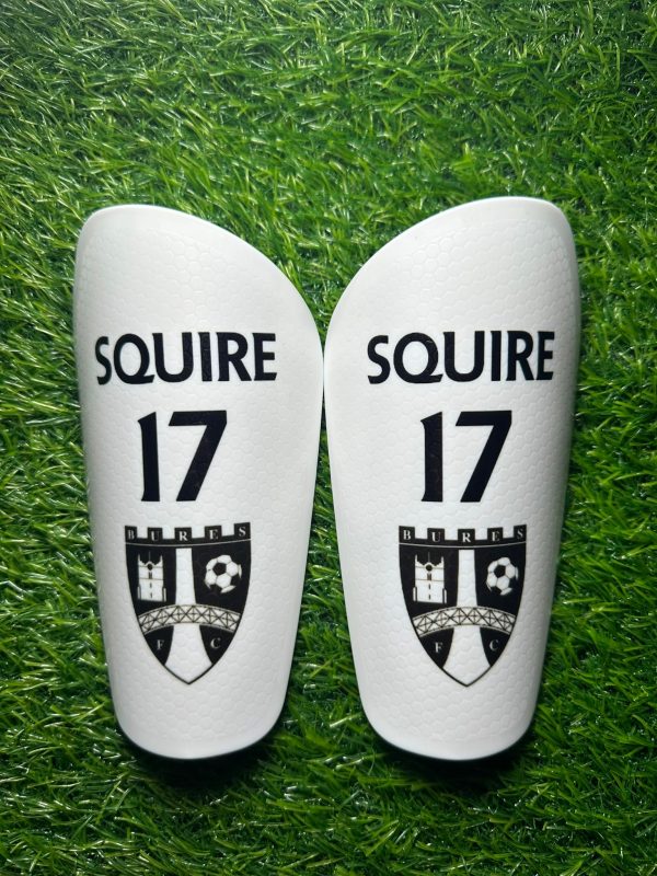 Standard personalised shin pads white backdrop black text and grassroots logo.